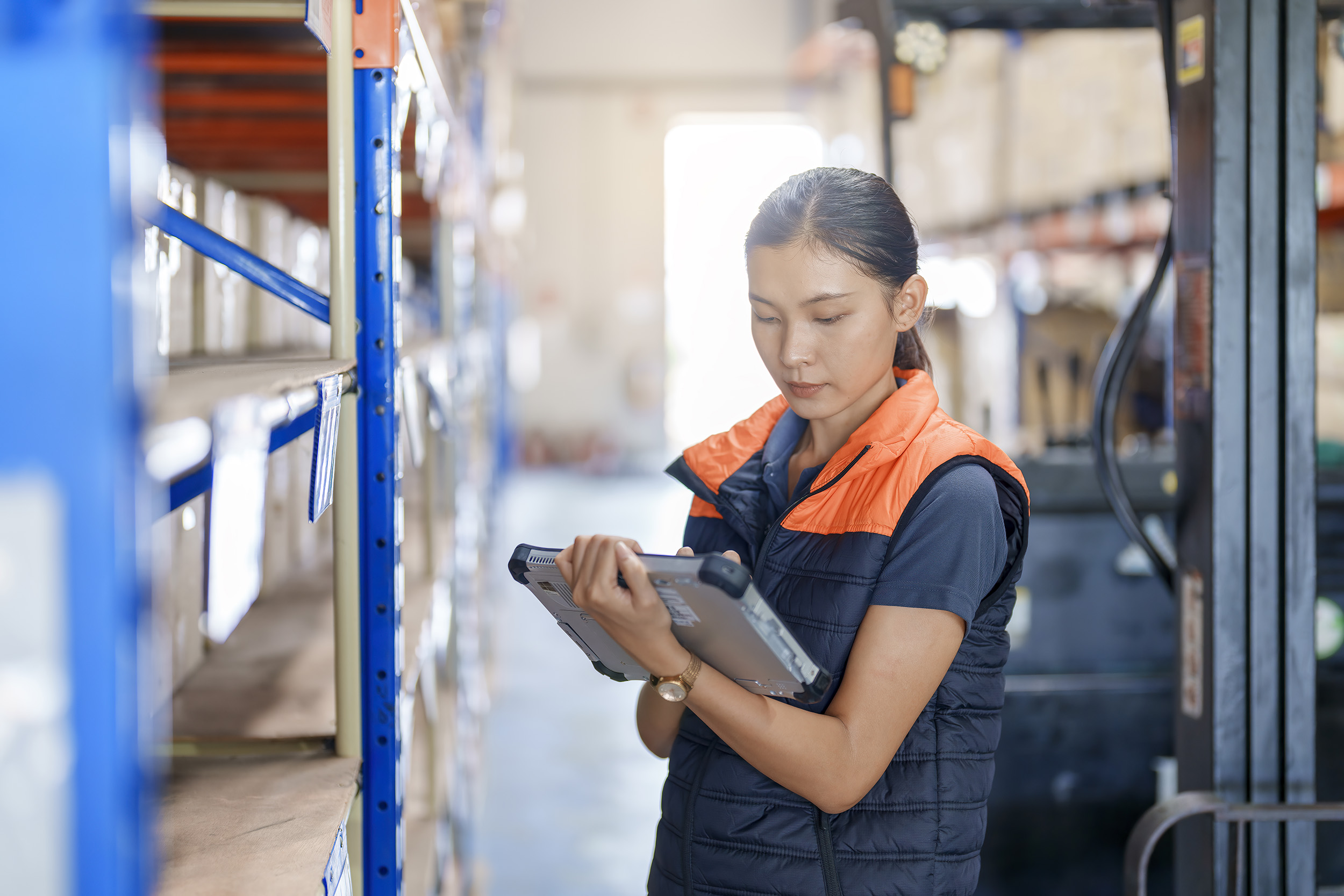 A warehouse worker makes inventory notes on an electronic tablet.