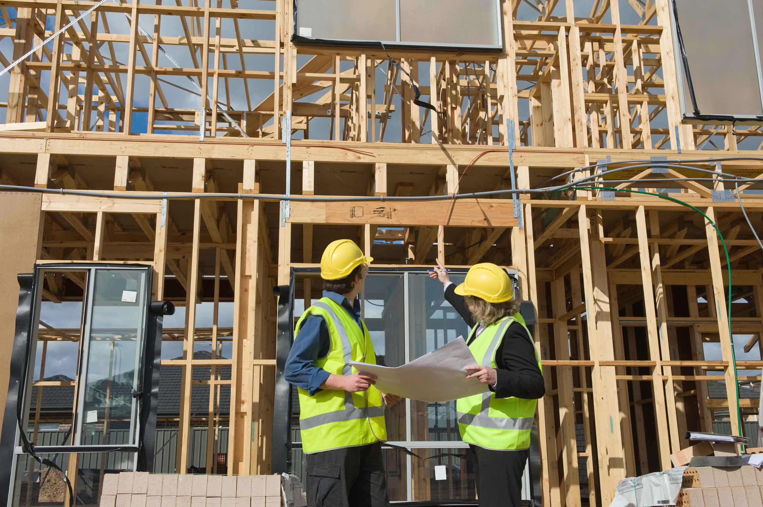 Two construction workers discuss a project in front of a framed building.