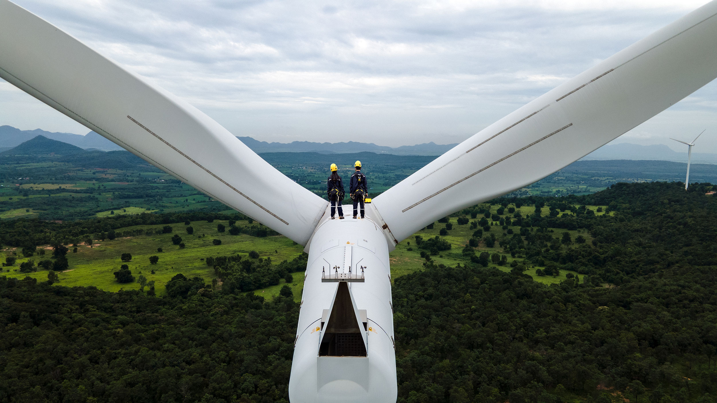 Two workers stand atop a giant modern windmill.